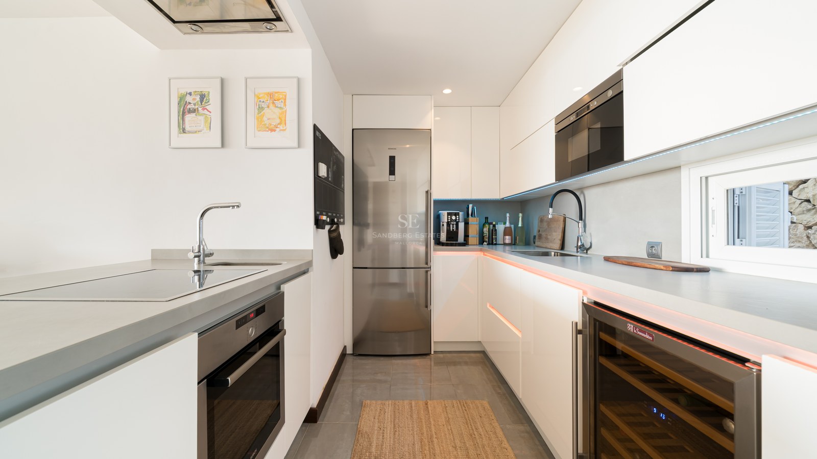 Cocina contemporánea blanca con electrodomésticos de acero inoxidable, vinoteca y encimeras de piedra gris.