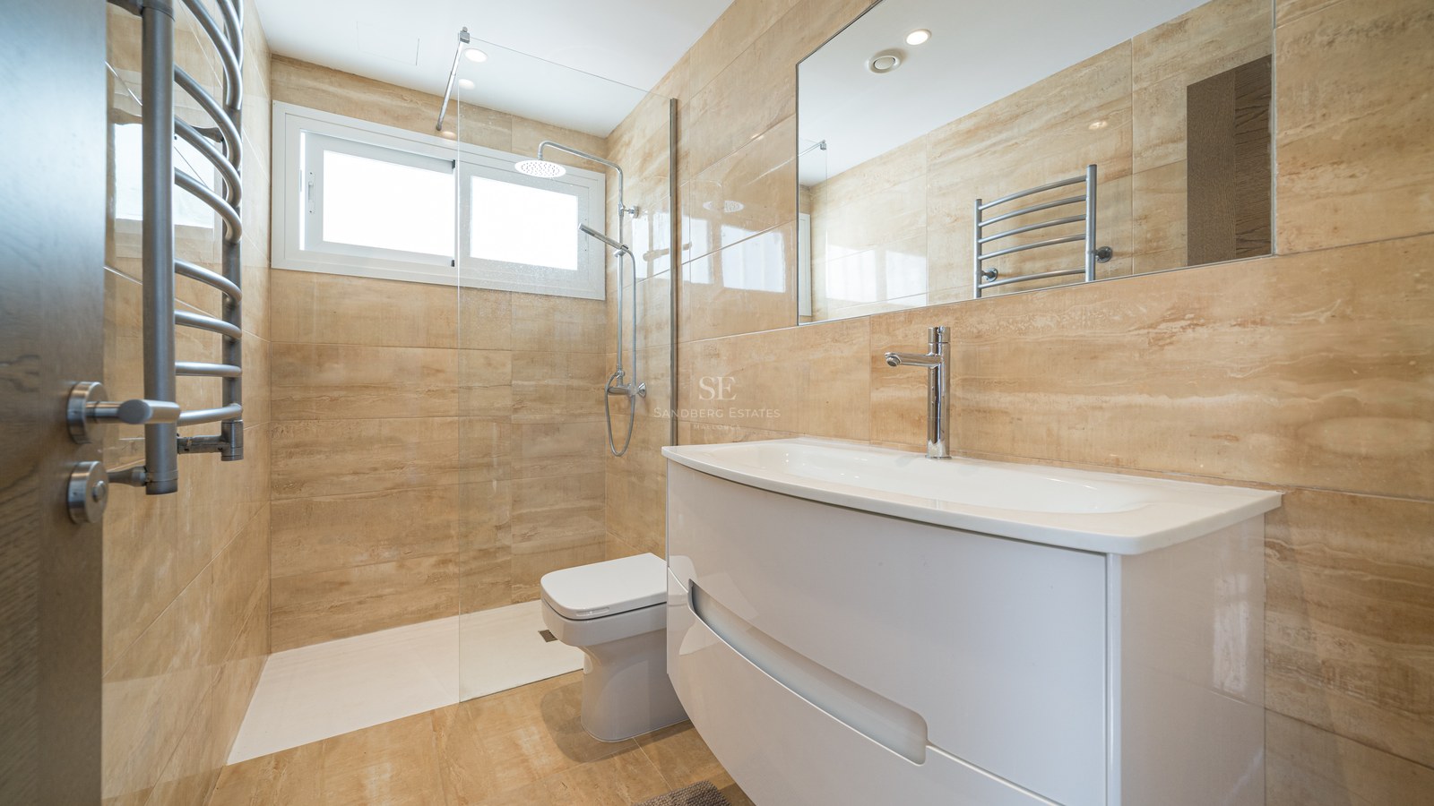Baño contemporáneo con azulejos beige, lavabo blanco, ducha de cristal y toallero calefactable.