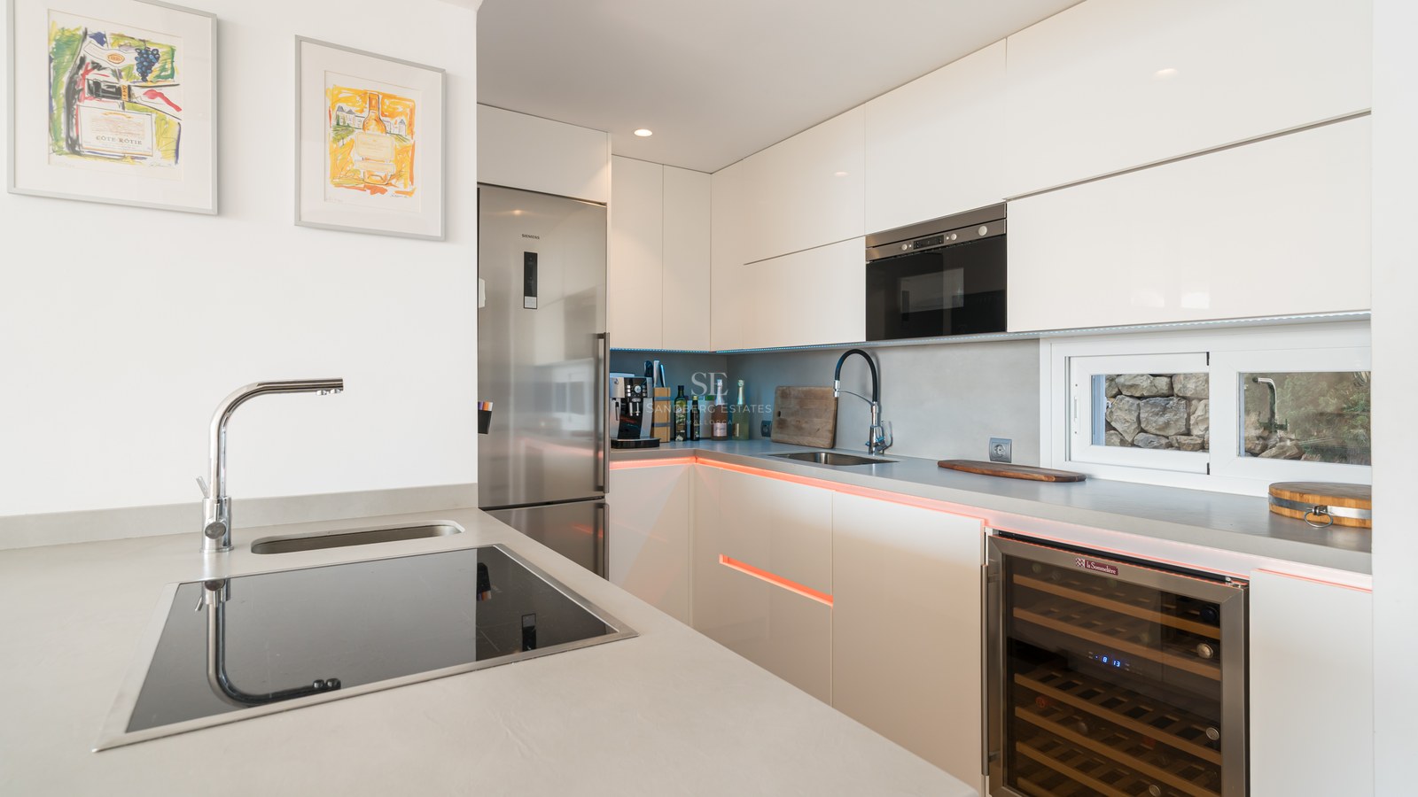 Cocina contemporánea blanca con armarios sin tiradores, vinoteca integrada y electrodomésticos Siemens de acero inoxidable.