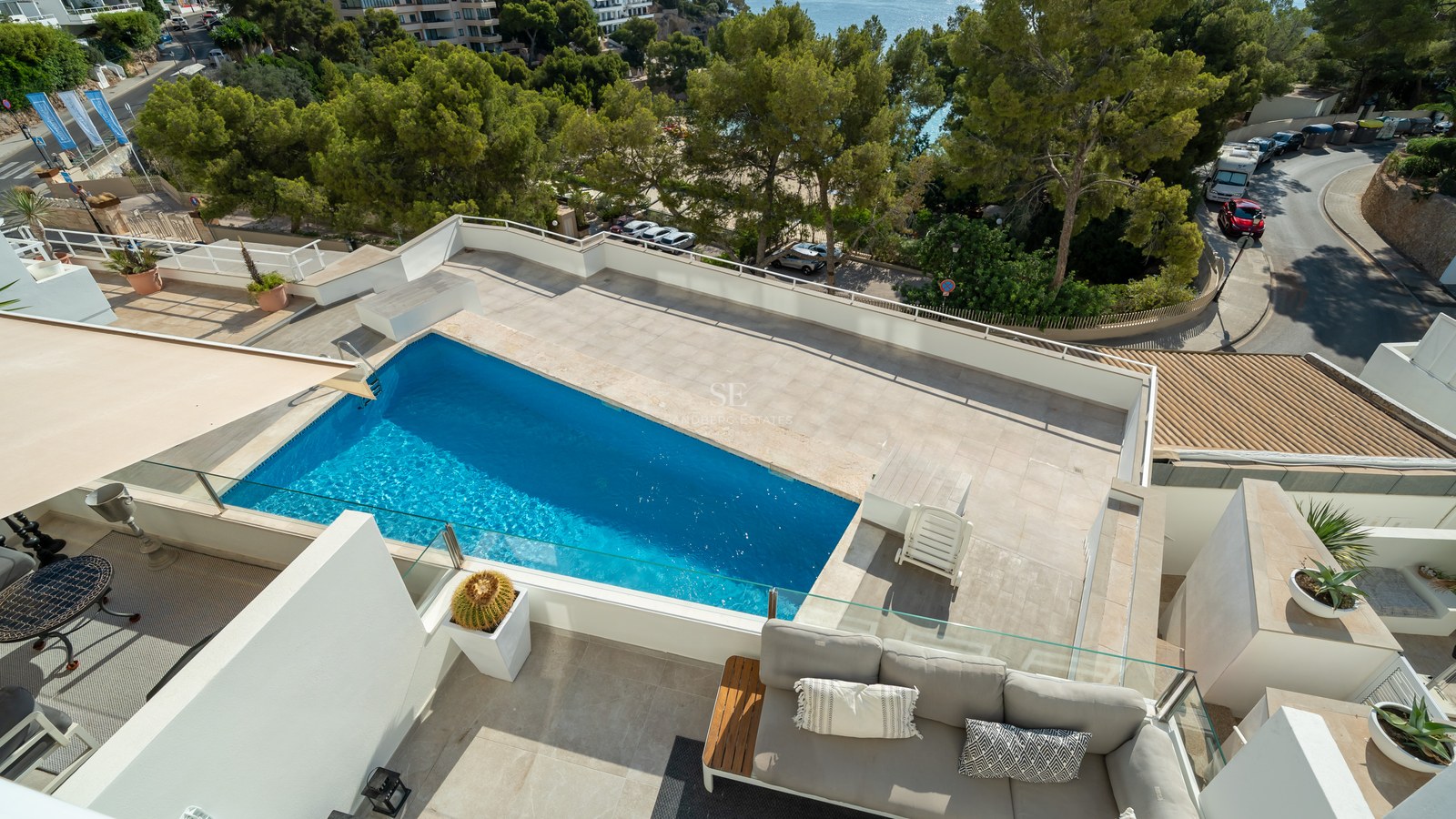 Terraza en la azotea con piscina azul, sofás de exterior y barandillas de cristal con vistas al entorno costero.