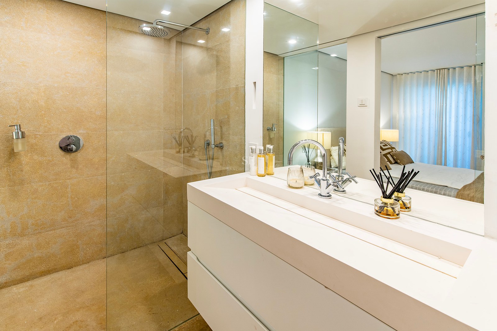 Salle de bains contemporaine avec vasque blanche, douche à l'italienne en pierre et reflet de la chambre dans le miroir.