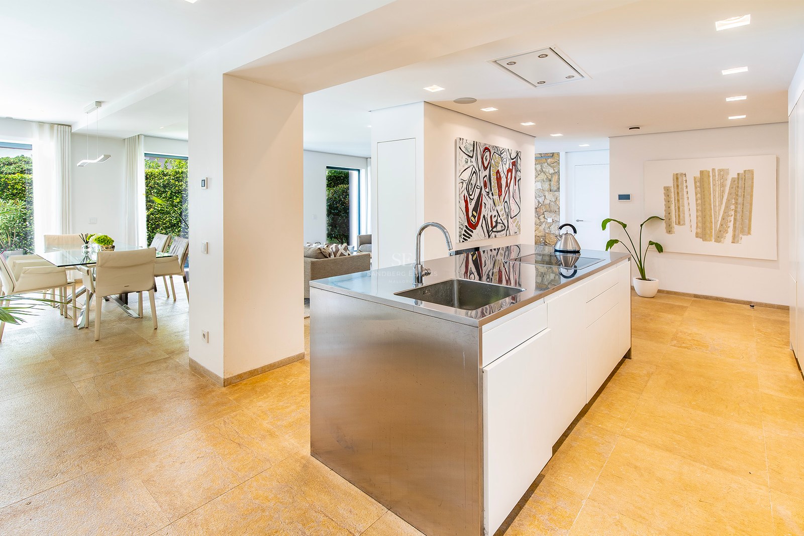Cuisine contemporaine avec îlot en acier inoxydable, sol en pierre naturelle et salle à manger lumineuse attenante.
