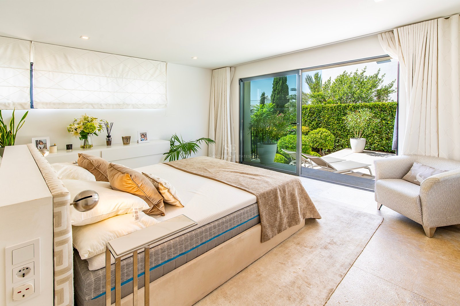 Chambre principale moderne avec baies vitrées coulissantes ouvrant sur un jardin privé luxuriant et une terrasse.