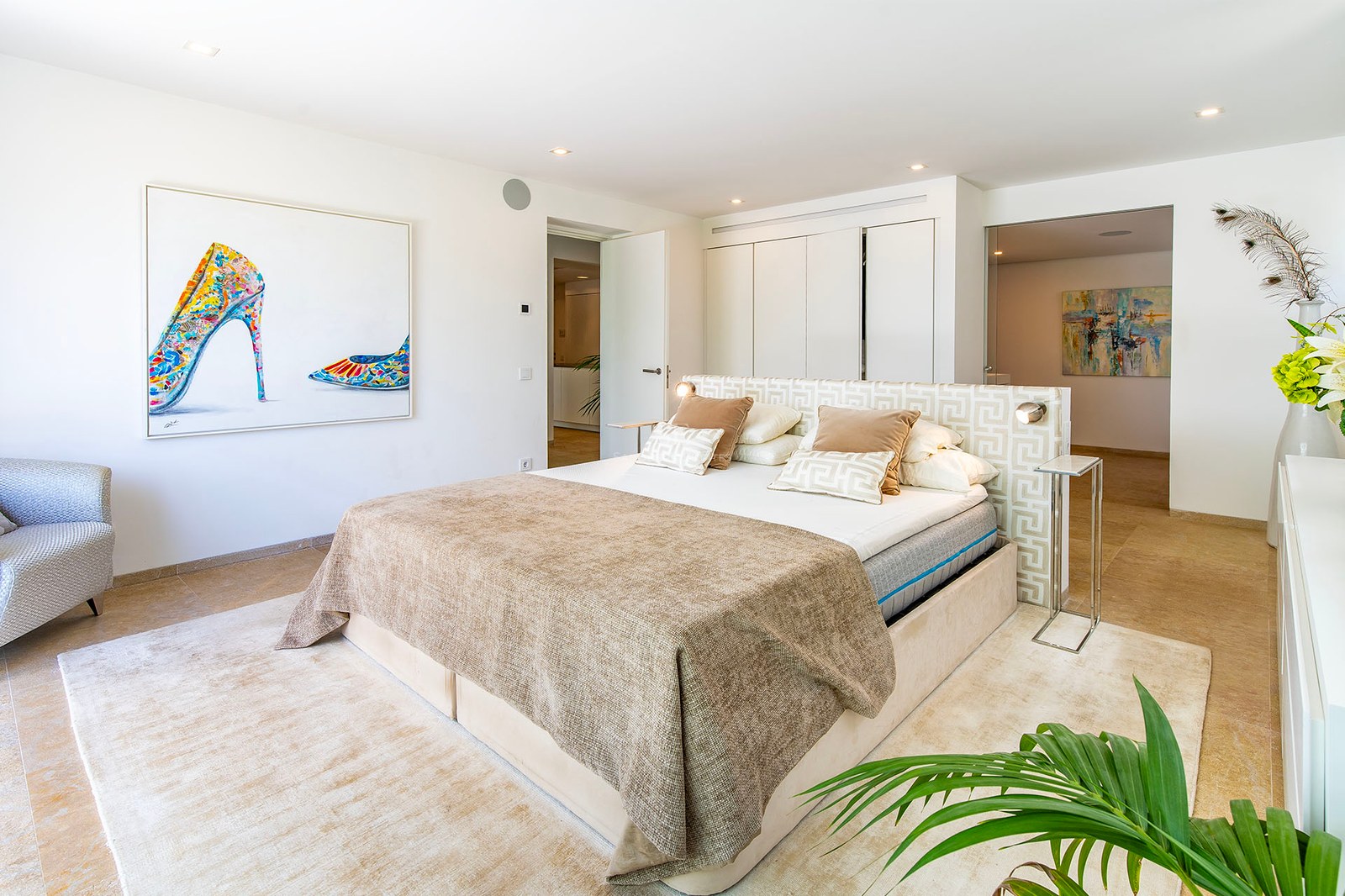 Chambre parentale moderne avec grand lit, sol en pierre naturelle, armoires intégrées et art mural coloré.