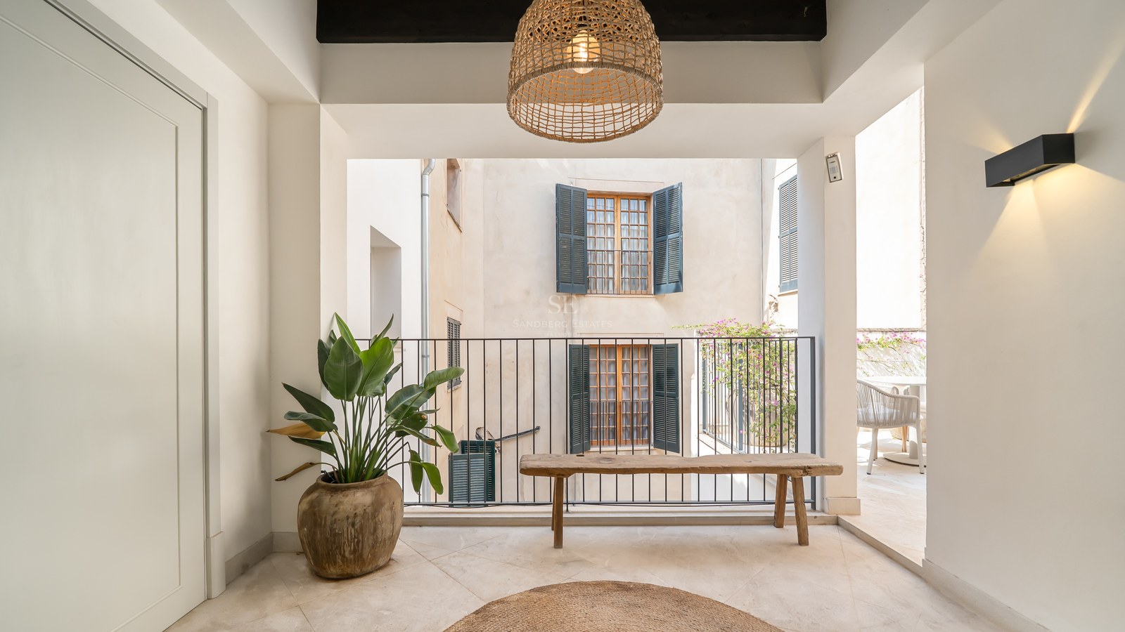 Covered terrace featuring a rustic wooden bench, large clay planter, and views of a traditional courtyard with shutters.