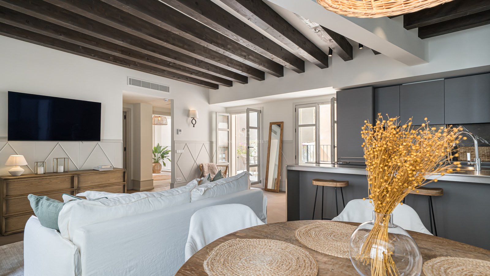 Open-plan living room with dark wood ceiling beams, a white linen sofa, and a modern charcoal grey kitchen.