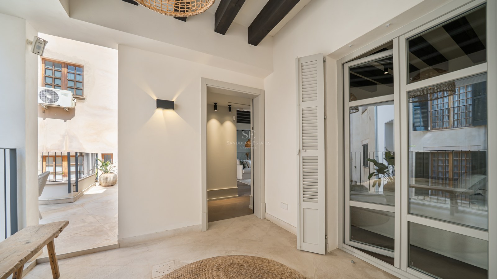 Covered terrace area with cream stone floors, dark ceiling beams, and a view into a modern interior.