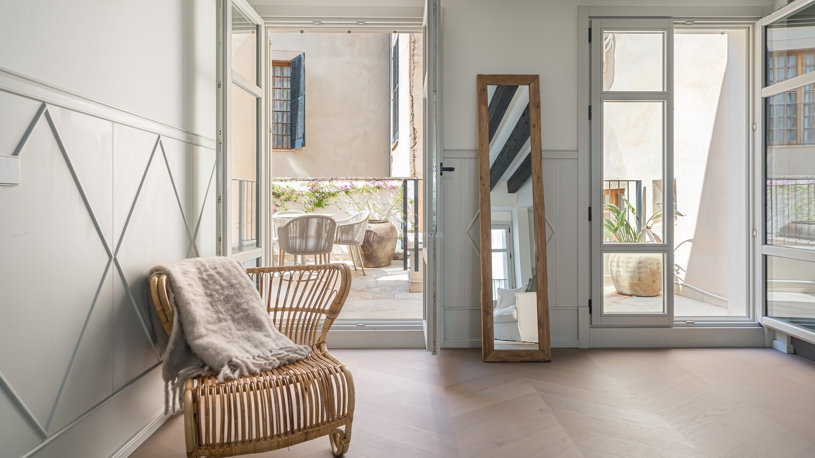 Interior room with chevron wood floors and open glass doors leading to a sun-drenched stone terrace.