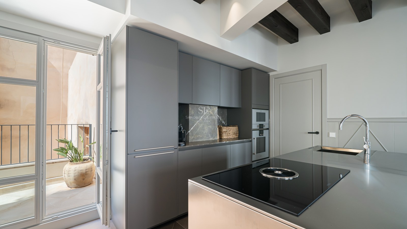 Contemporary charcoal grey kitchen featuring an island with induction hob, marble splashback, and balcony access.