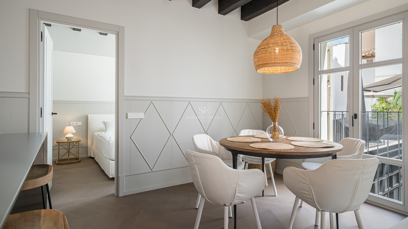 Modern dining room with round wooden table, white chairs, and woven pendant light next to a bedroom entrance.