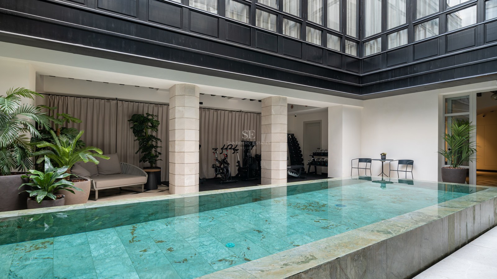 Heated indoor swimming pool with turquoise tiling adjacent to a private gym area with spin bikes and weights.