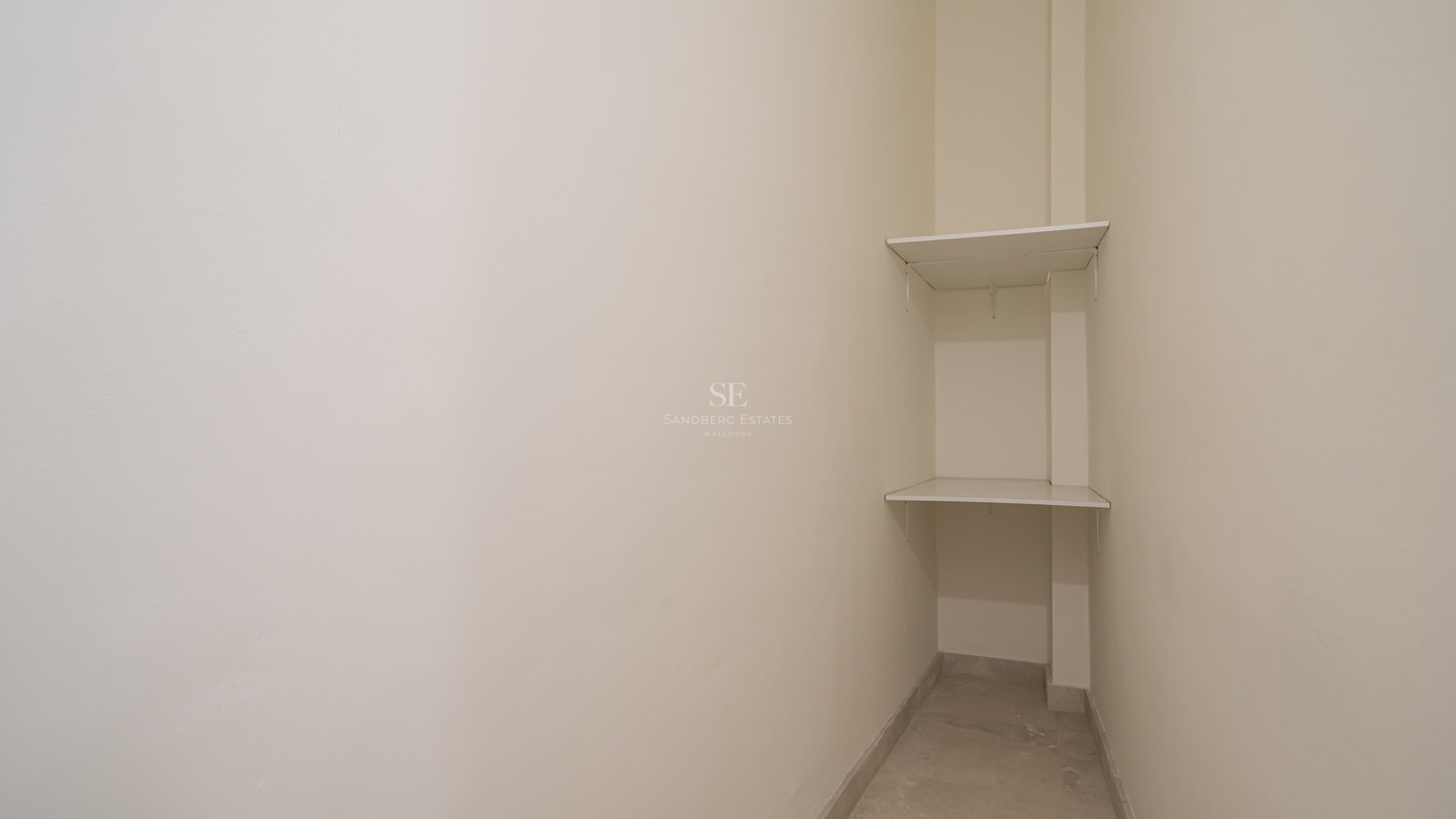A small corner storage space featuring two white shelves against cream-colored walls and light tiled flooring.