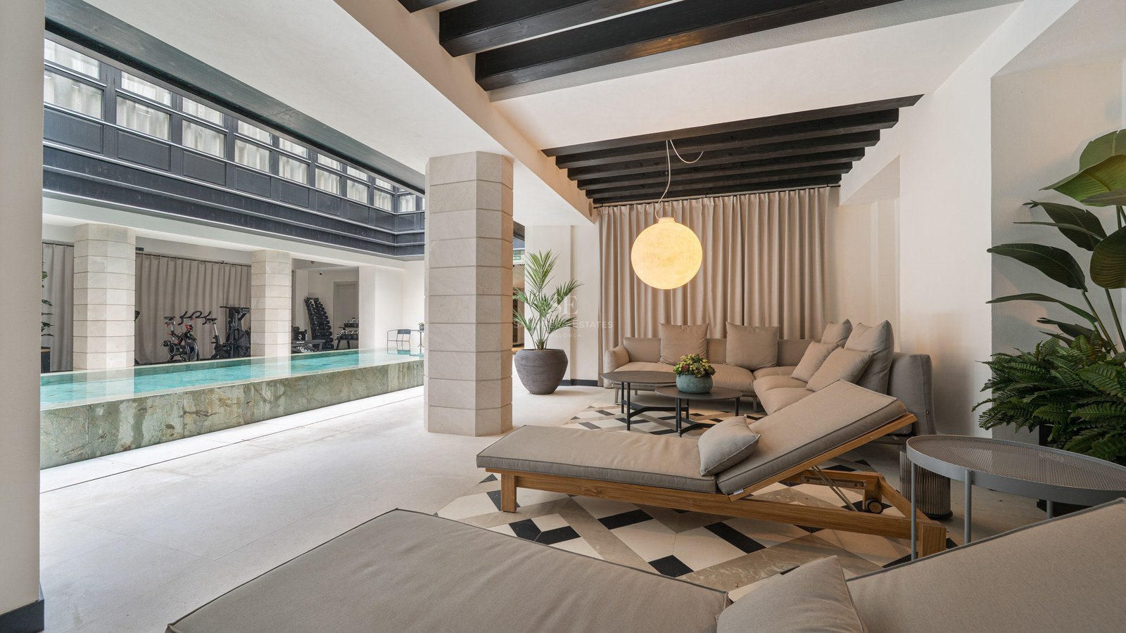 Relaxation lounge with sofas and daybeds next to an indoor lap pool with a fitness area in the background.