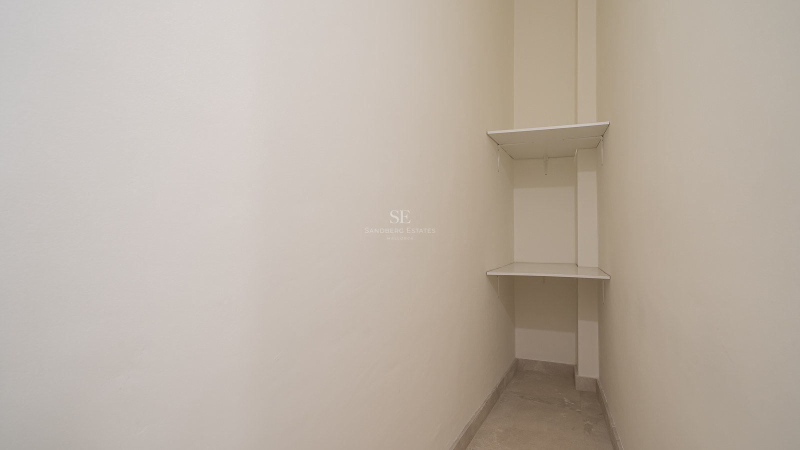 Narrow off-white storage area with two white shelves in a corner and light stone flooring.