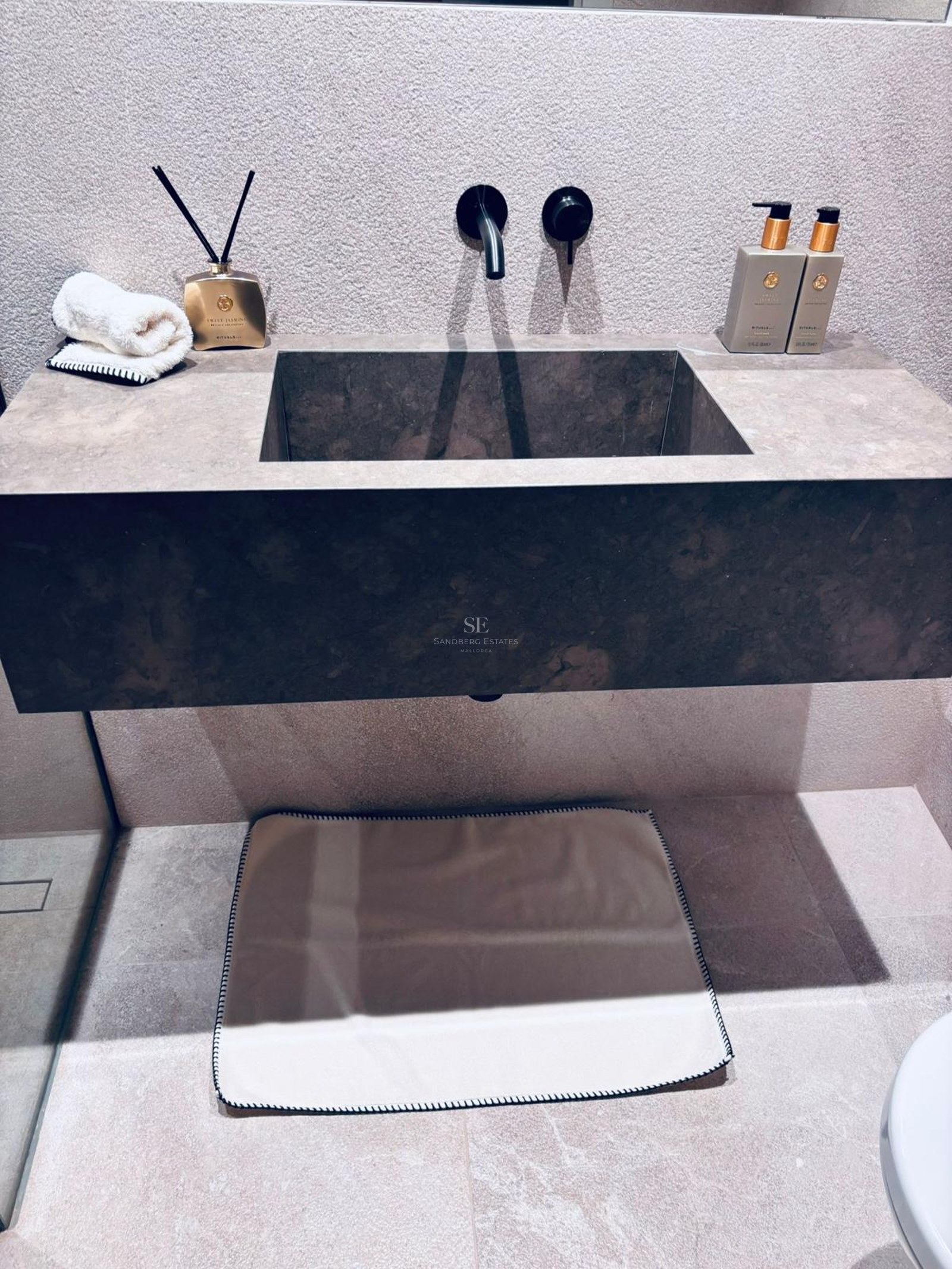 Close-up of a dark natural stone floating sink with matte black wall-mounted taps and textured stone walls.
