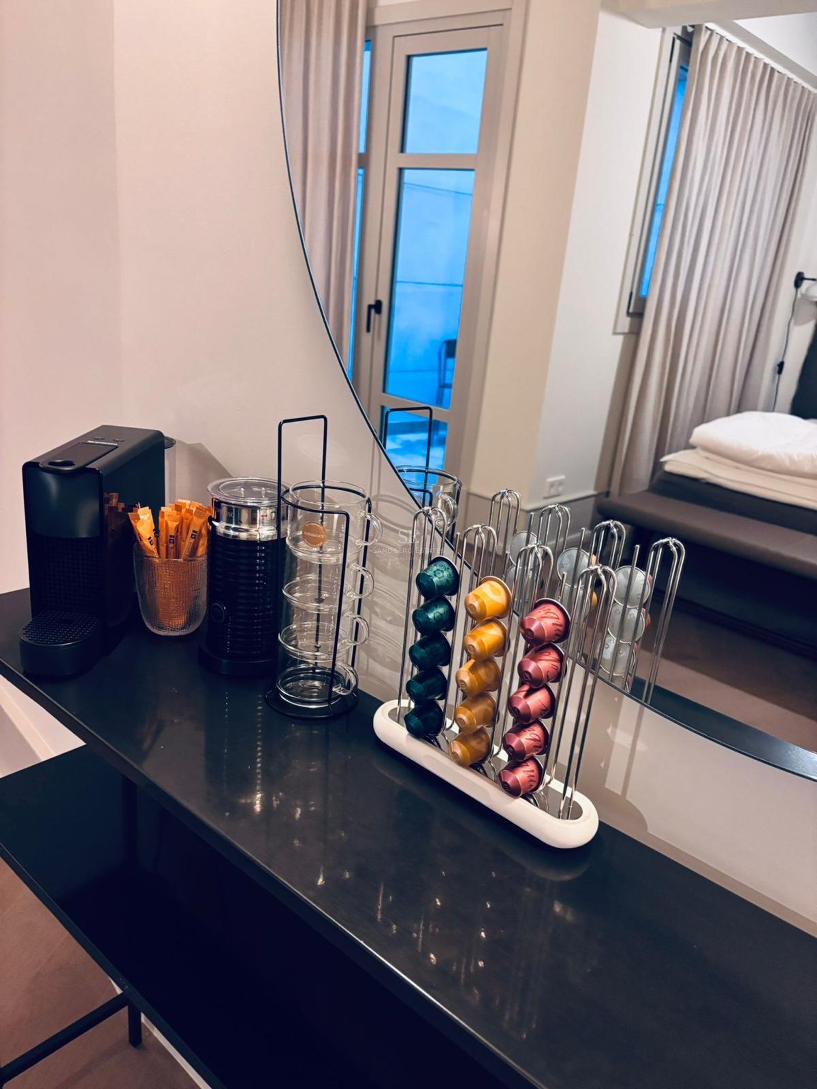 Black console with a Nespresso machine, milk frother, and capsule holder reflected in a round mirror.