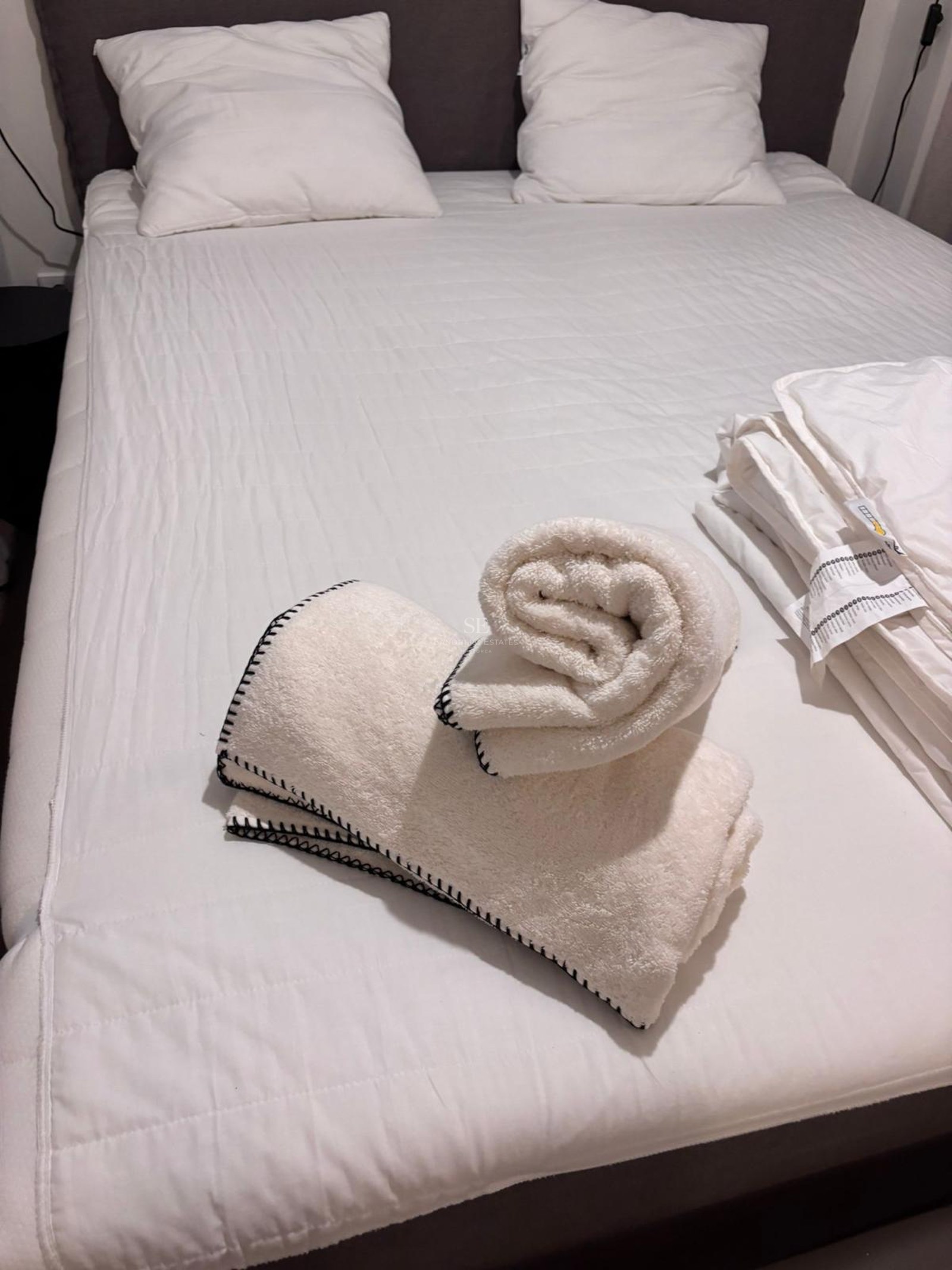 Close-up of a bed with white quilted duvet and plush towels featuring black stitched edges in a modern bedroom.