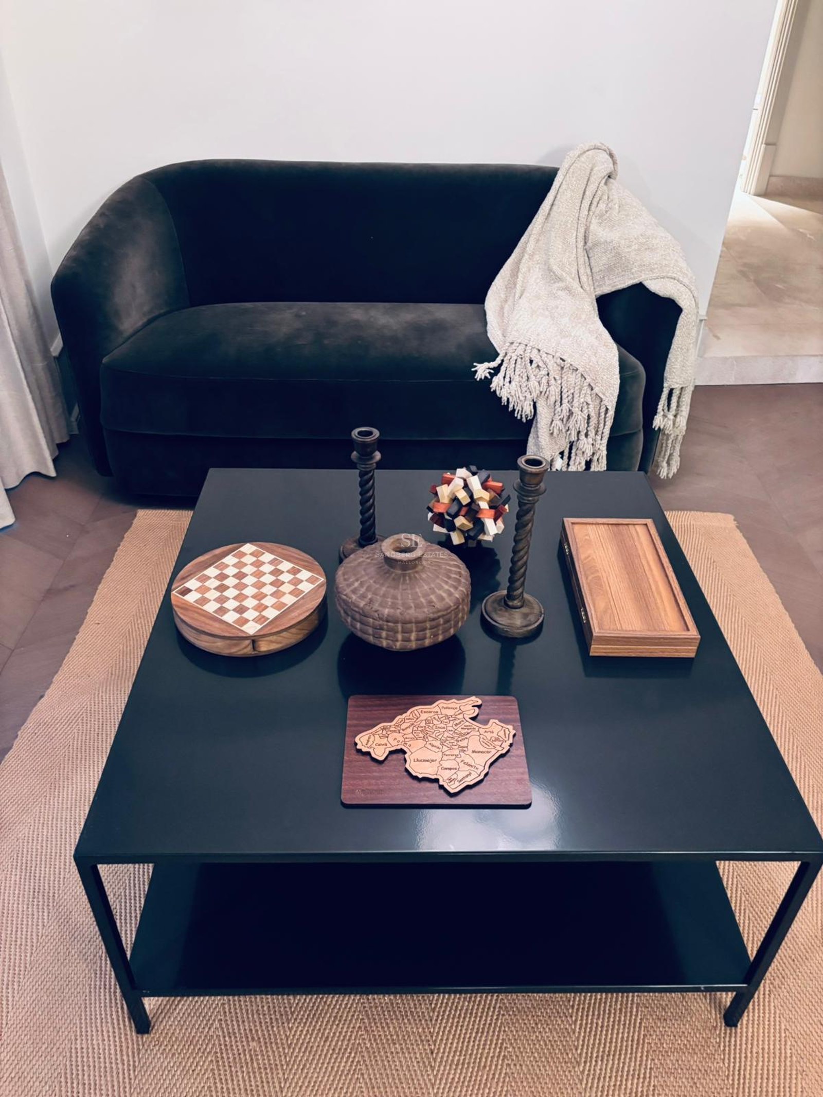 A black square coffee table featuring wooden decorative items including a Mallorca map and chess set.