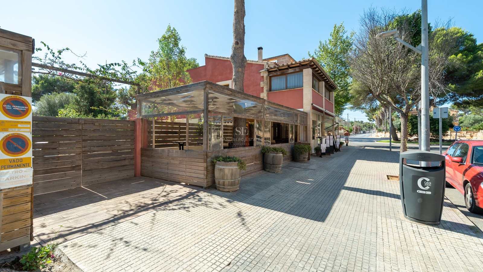 Fachada de edificio terracota con terraza de madera cerrada en una acera soleada de Calvià.