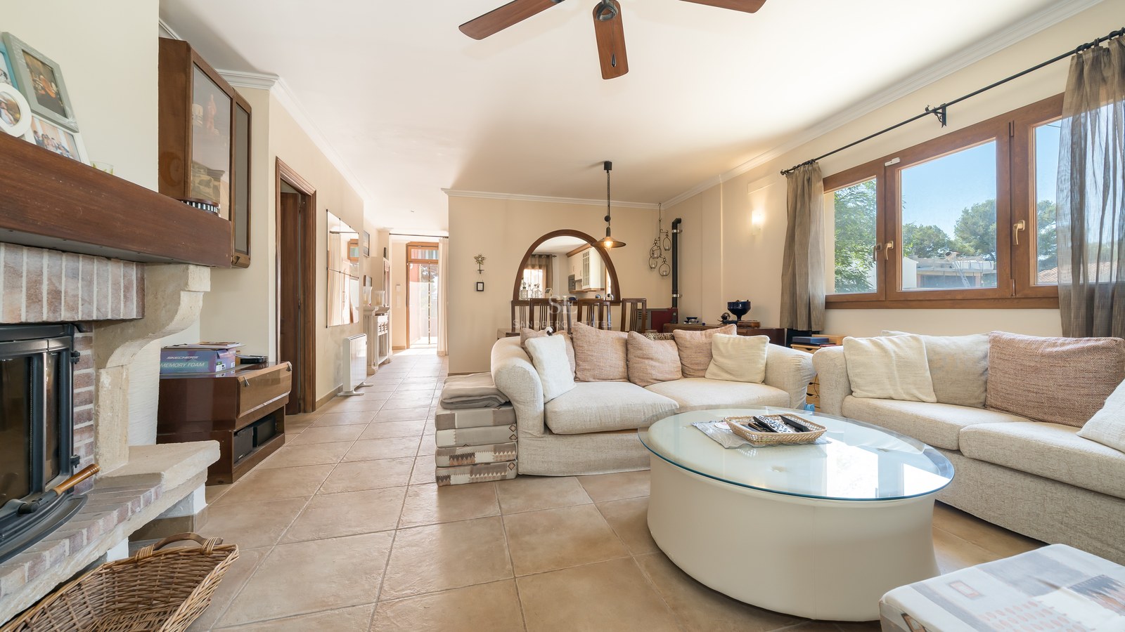 Salón acogedor con suelos de terracota, sofás crema, mesa de centro de cristal y chimenea de leña.