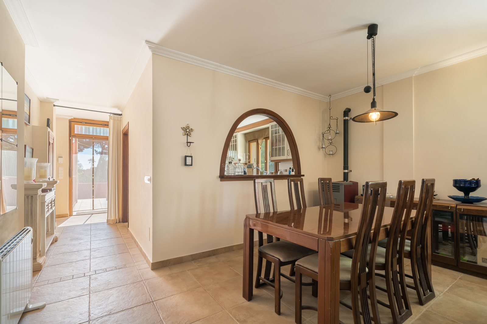 Comedor con mesa de madera oscura, suelos de terracota y un arco con vista a la cocina en una villa luminosa.