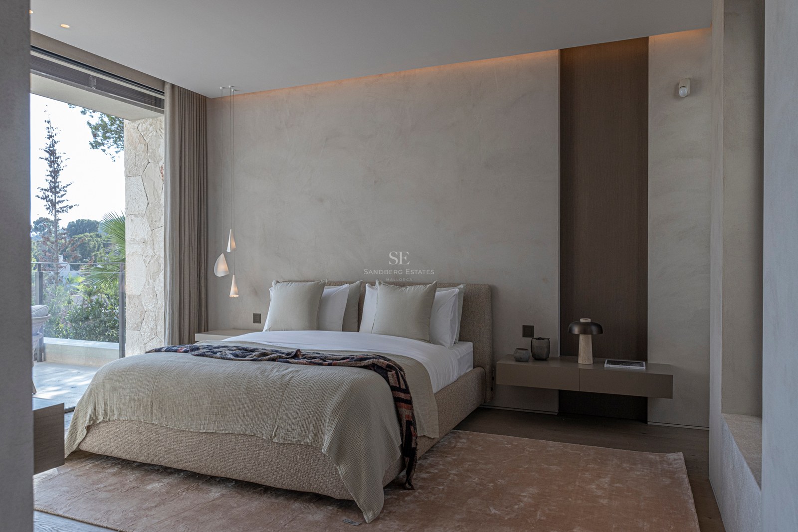 Chambre principale moderne, tons neutres, murs texturés, grandes baies vitrées donnant sur une terrasse en pierre.