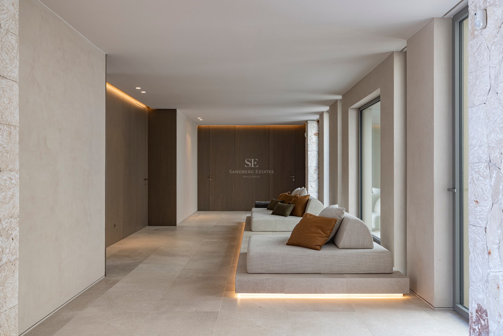 Salon minimaliste avec banquettes basses, murs en pierre naturelle et éclairage LED indirect chaleureux.