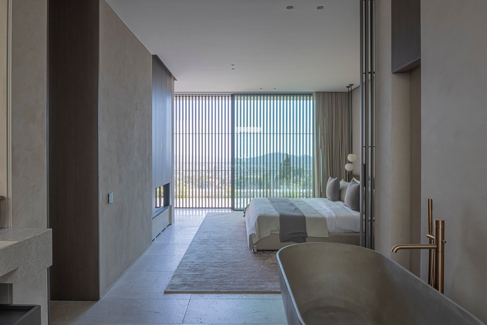 Chambre principale moderne avec baignoire en pierre, baies vitrées avec persiennes en bois et cheminée.