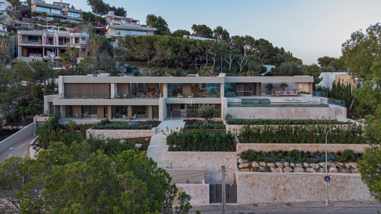 Villa moderne à plusieurs niveaux avec murs en pierre, jardins en terrasses et piscine à débordement à flanc de colline.
