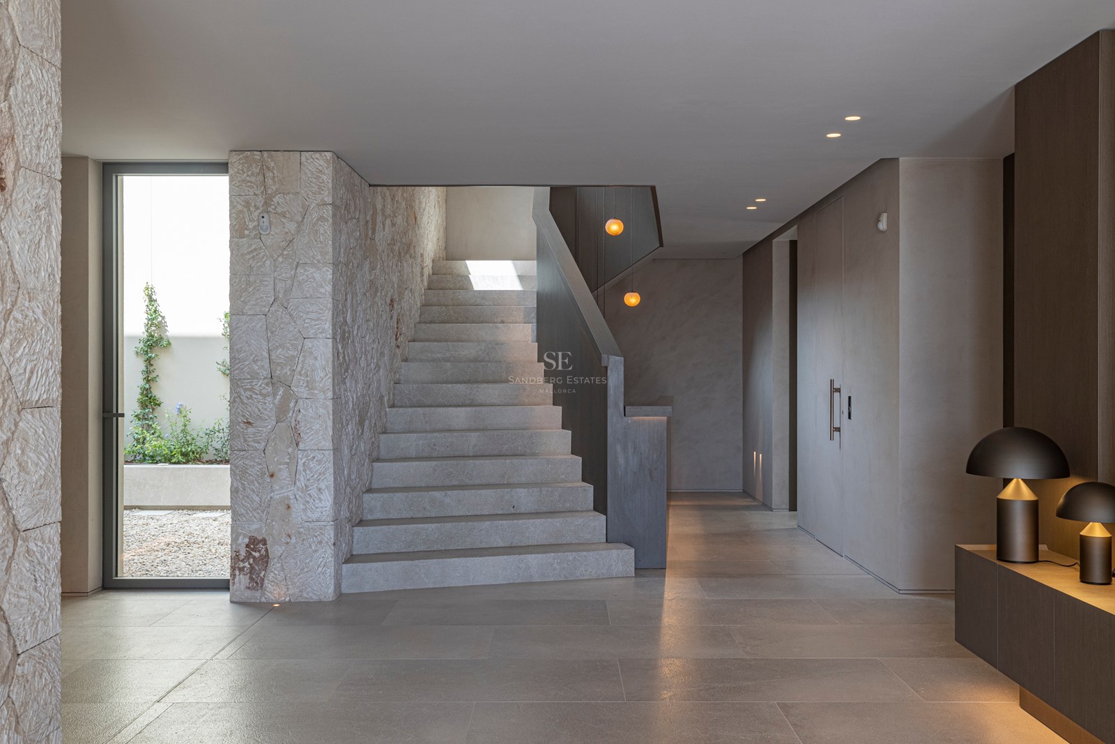 Couloir moderne avec escalier en pierre, murs en pierre texturée et éclairage design chaleureux.