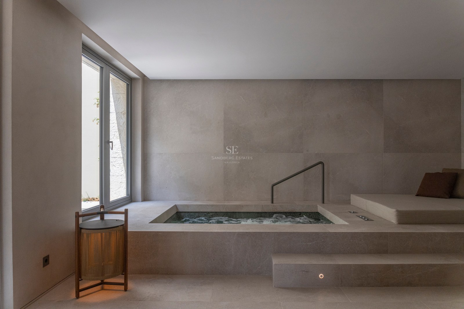 Spa intérieur en pierre avec piscine d'hydromassage encastrée, lit de repos et lumière naturelle.