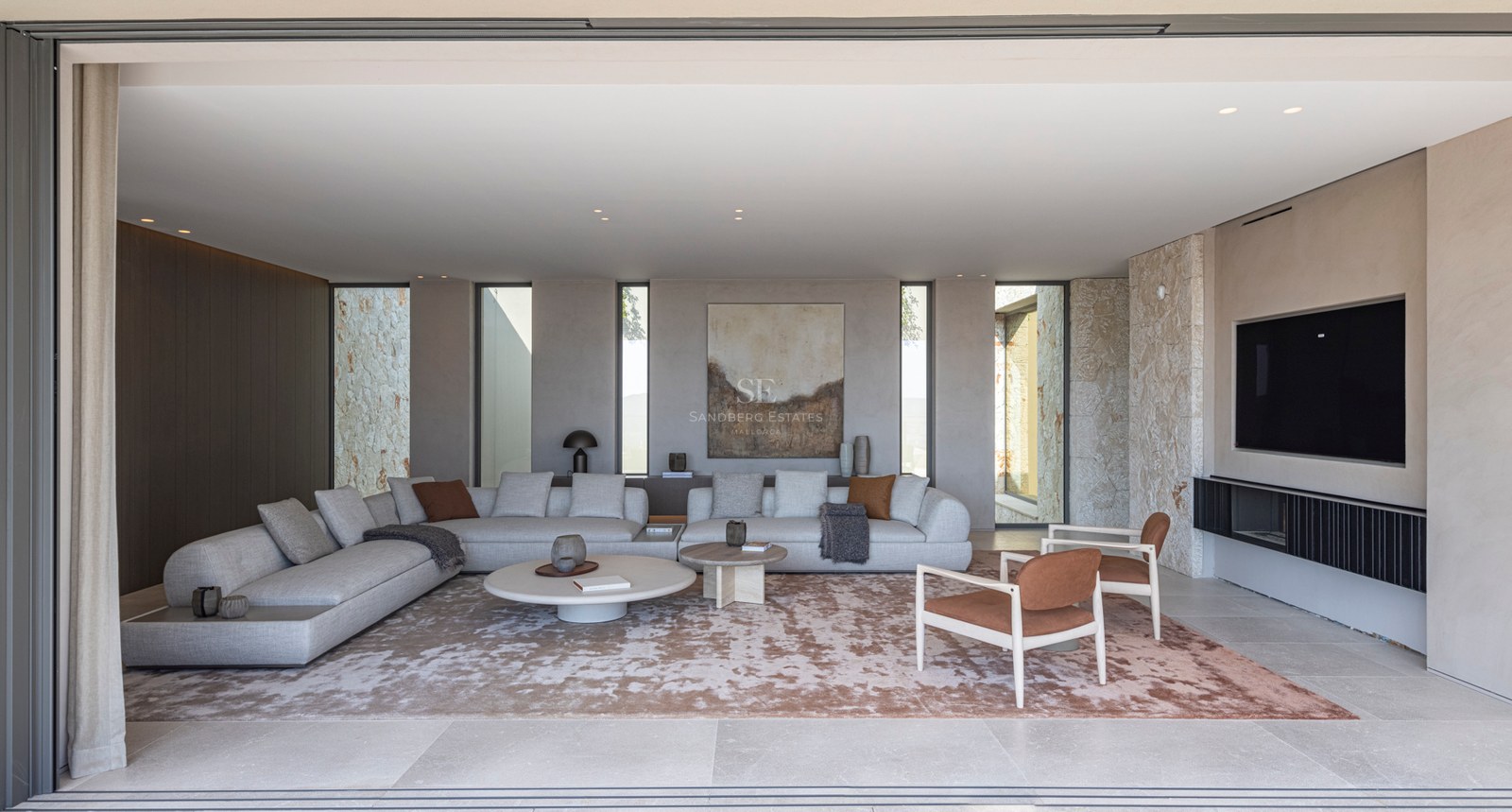 Un salon spacieux et moderne avec des canapés gris, un mur en pierre naturelle et de grandes baies vitrées.