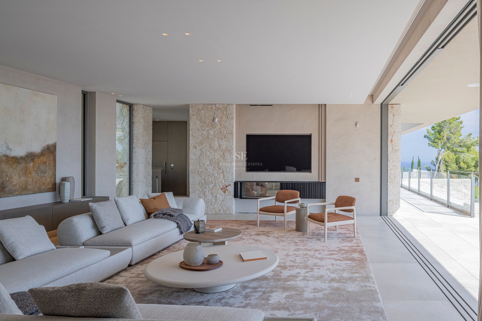 Salon minimaliste avec murs en pierre, canapé gris et baies vitrées coulissantes ouvrant sur une terrasse.