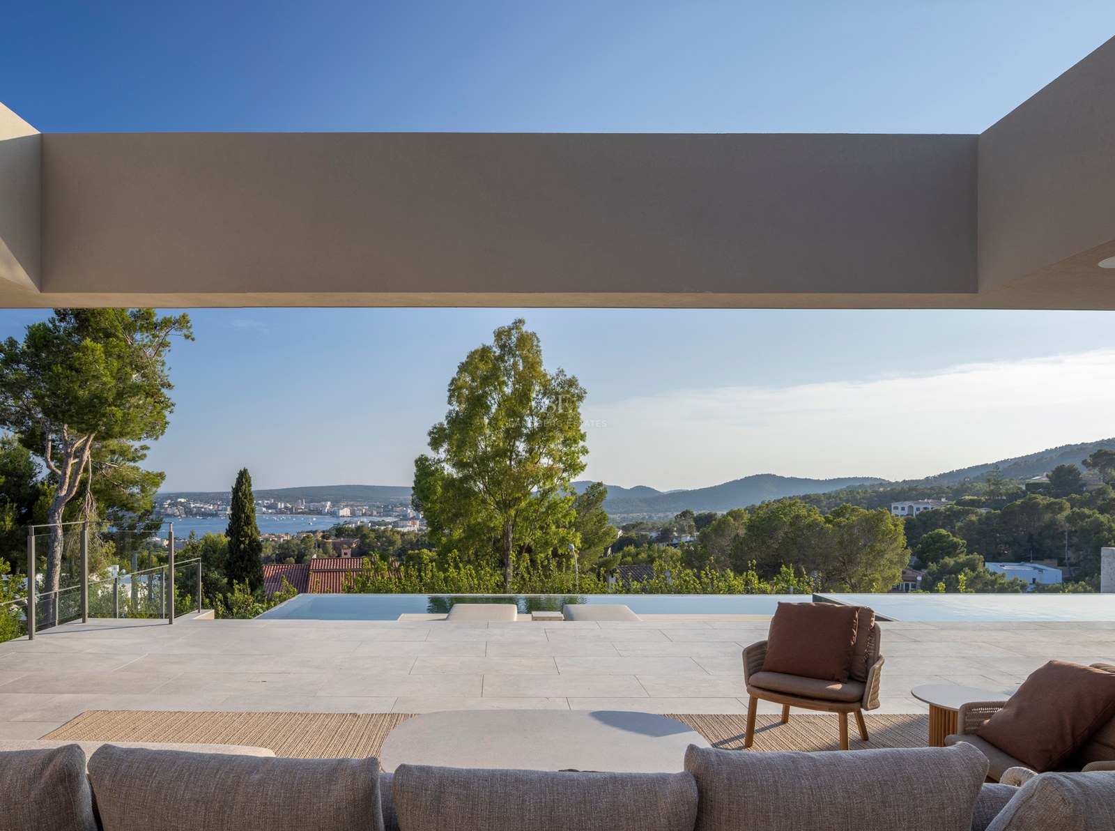 Salon extérieur de luxe avec mobilier contemporain sur une terrasse en pierre dominant la piscine et la mer.