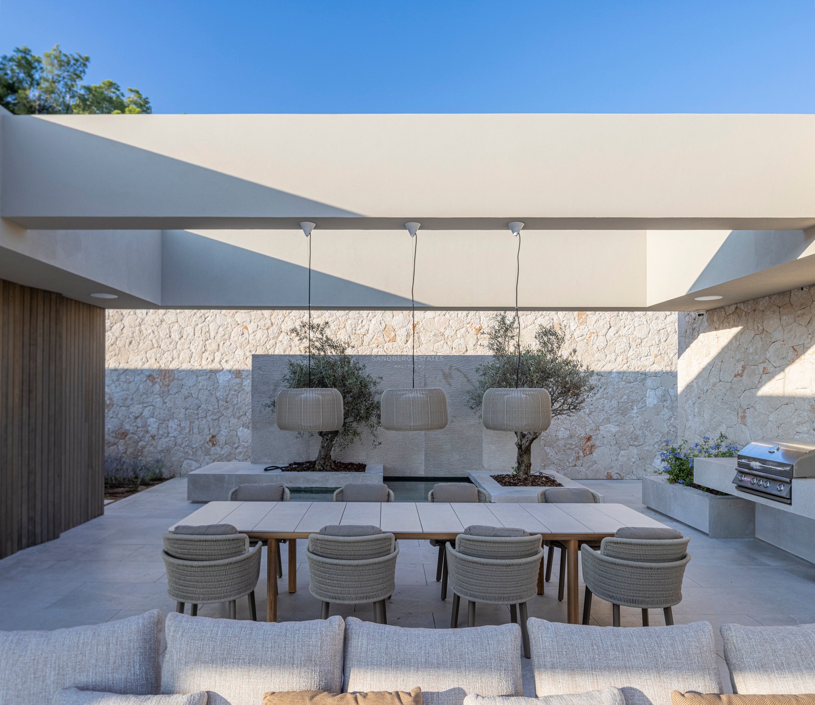 Terrasse moderne avec une grande table en bois, des chaises tressées, des suspensions design et un barbecue intégré.