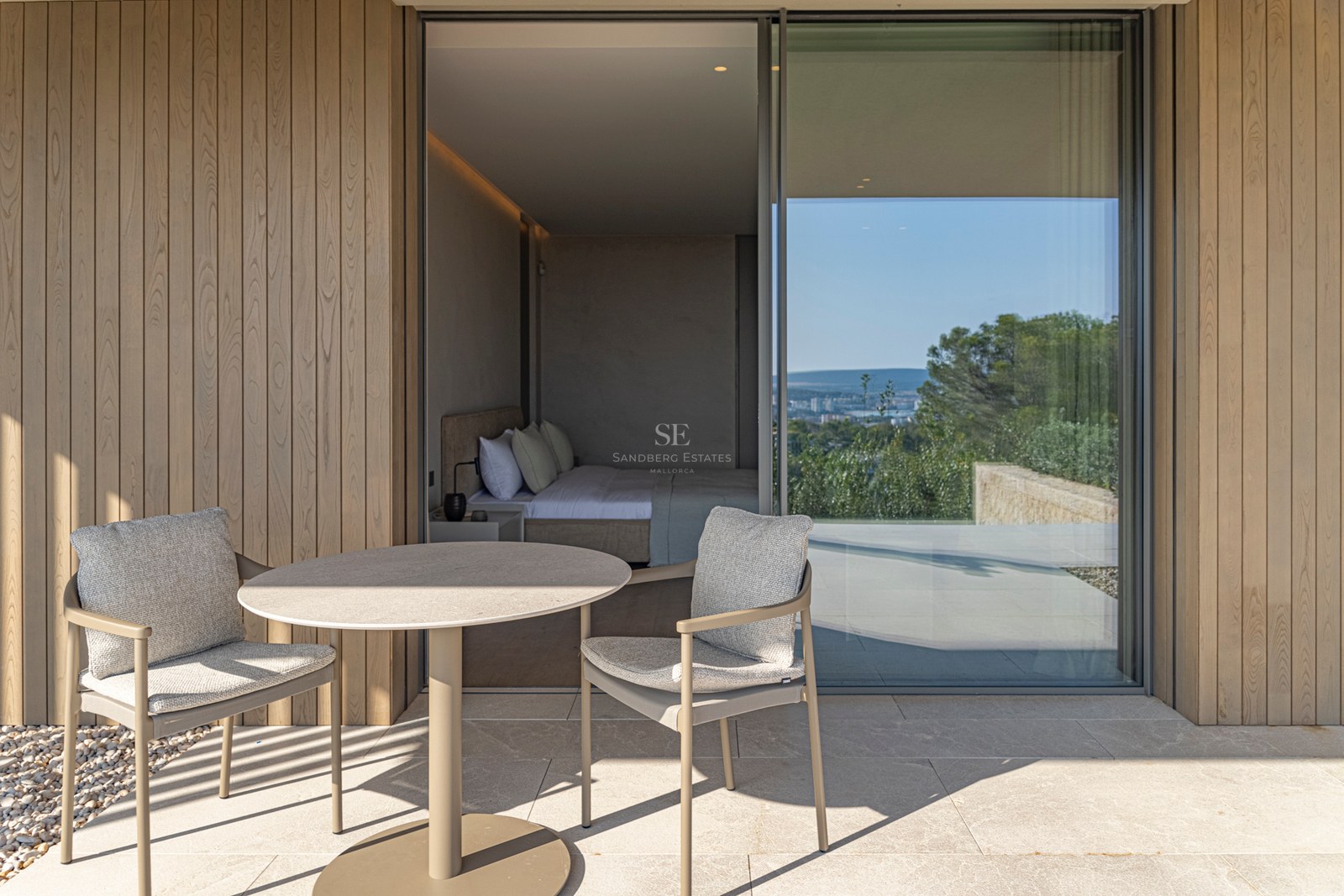 Table et chaises design sur une terrasse en pierre naturelle devant de grandes baies vitrées et des murs en bois.