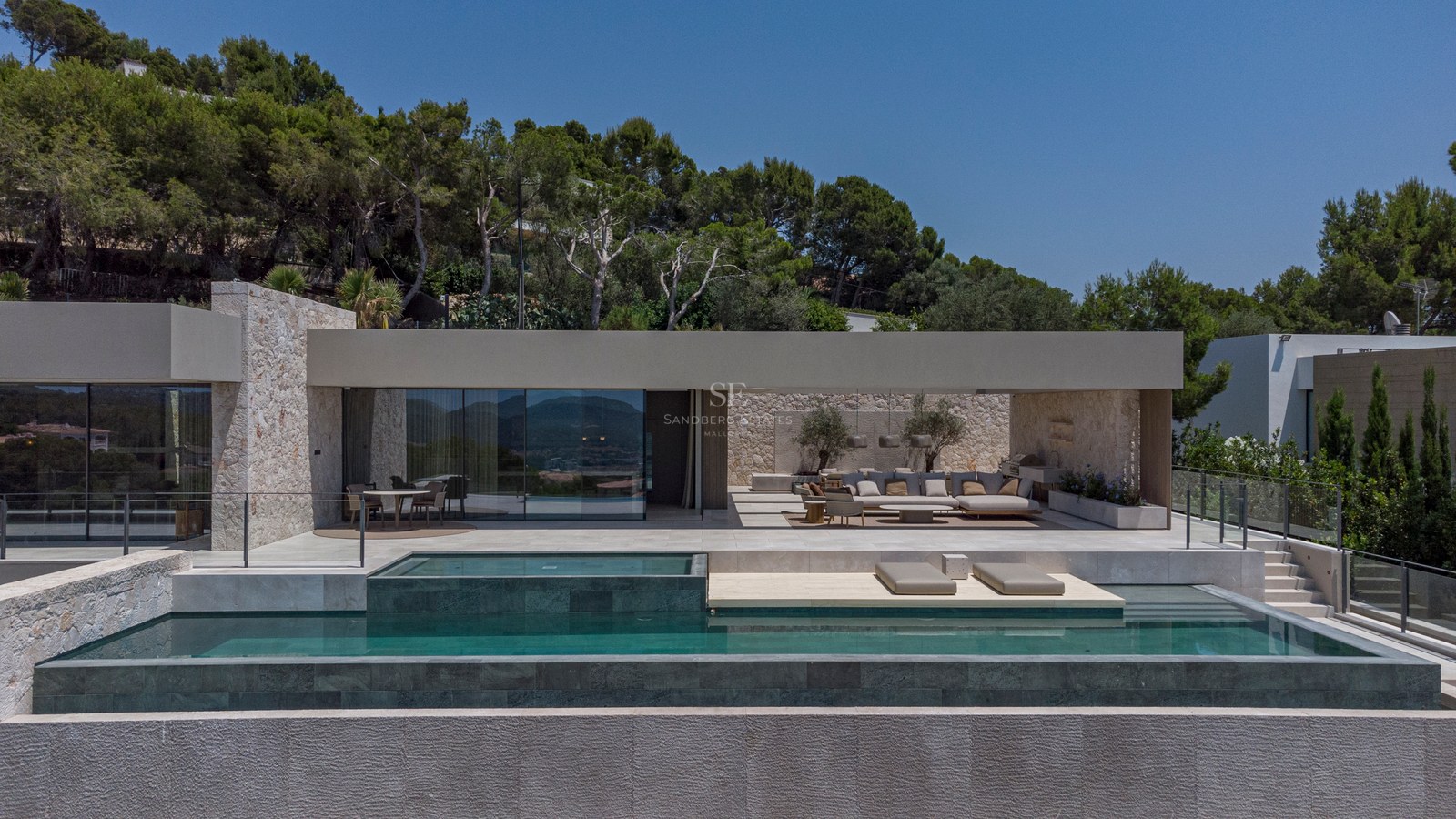 Extérieur d'une villa contemporaine avec piscine à plusieurs niveaux, terrasse couverte et murs en pierre naturelle.