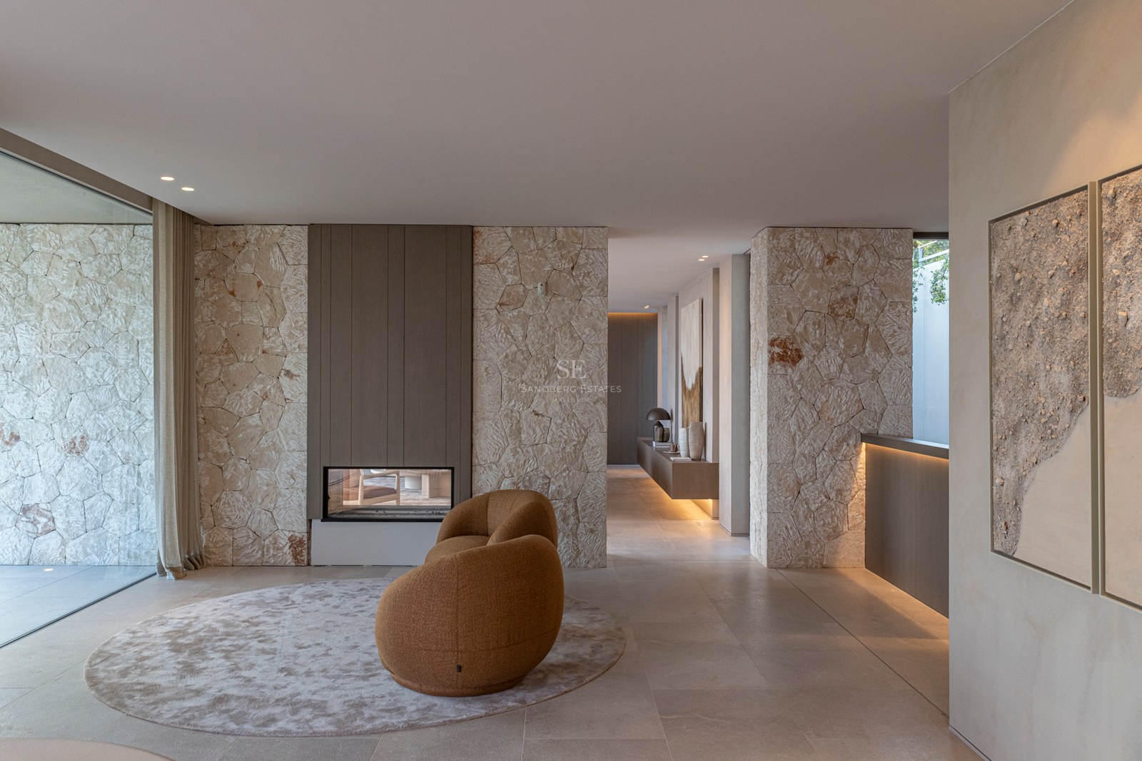 Espace de vie moderne avec cheminée double face en pierre, fauteuil incurvé et grandes baies vitrées.