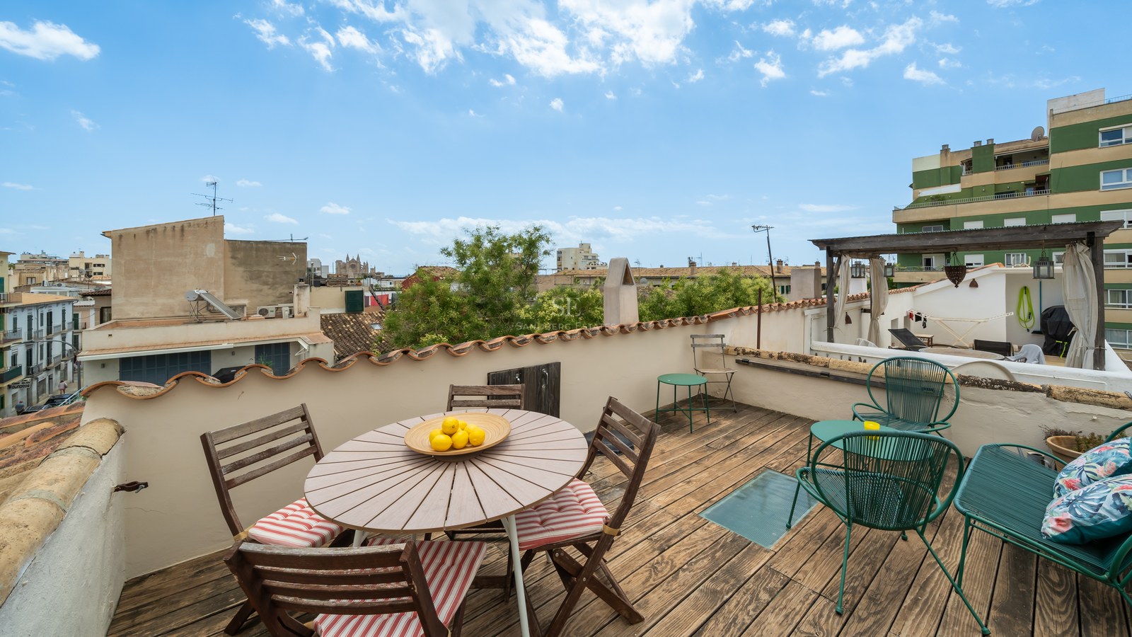 Terraza de madera en azotea con mesa de comedor, sillas de metal verde y vistas panorámicas de Palma y la catedral.