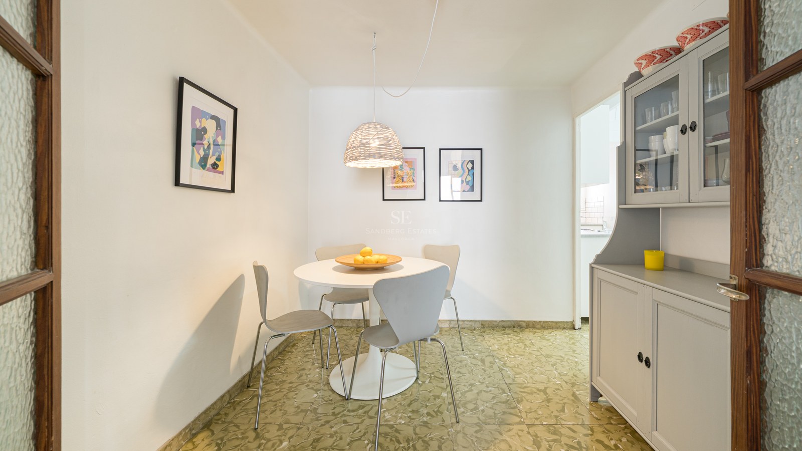 Zona de comedor luminosa con mesa redonda blanca, sillas grises modernas y suelo de baldosa verde estampada.