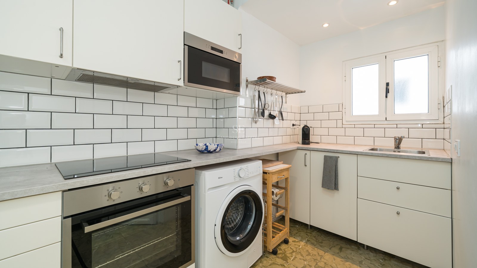Cocina blanca moderna con azulejos tipo metro, horno integrado, placa de inducción y lavadora bajo encimera.
