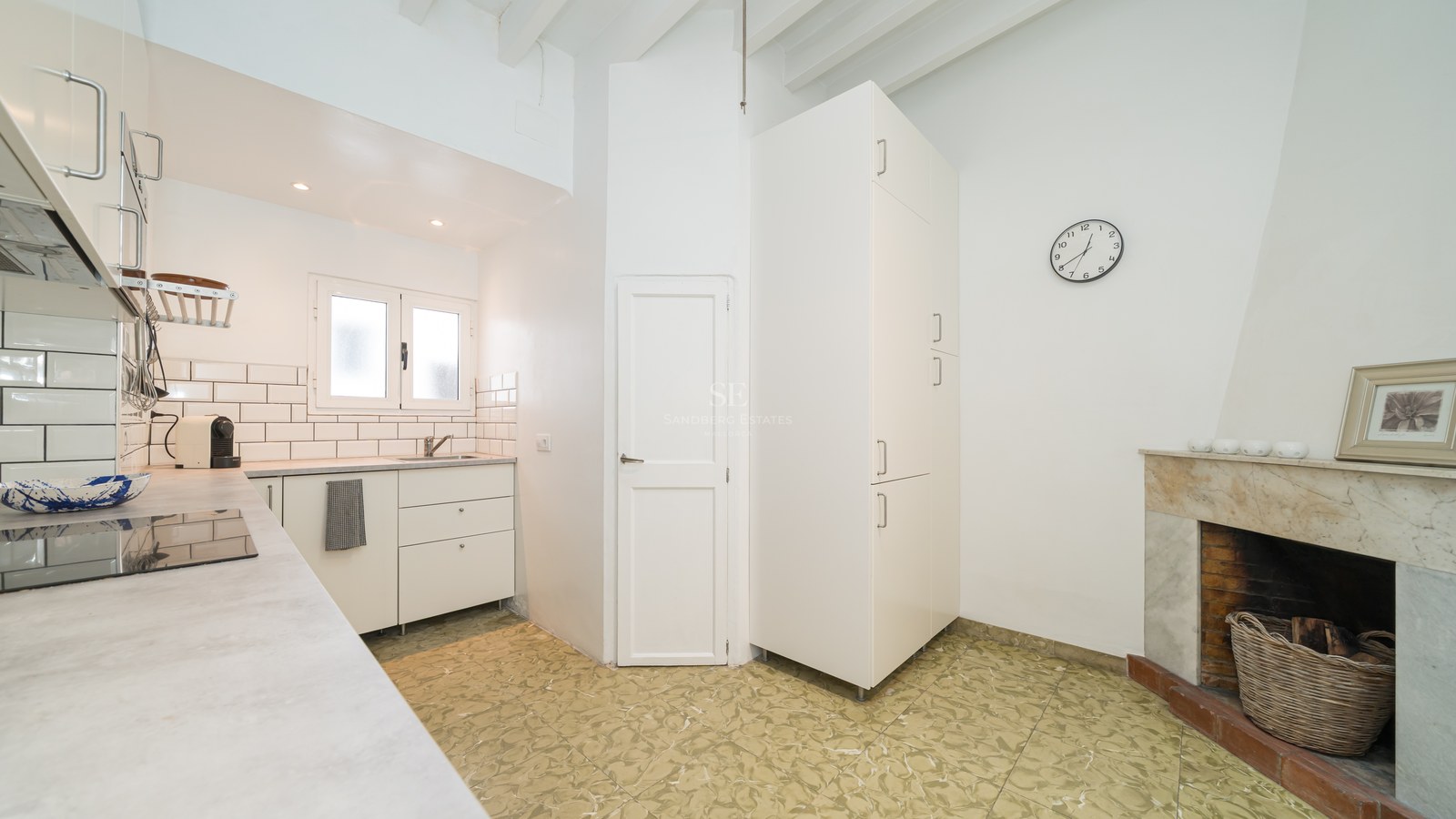 Cocina blanca moderna con chimenea de mármol, techos de vigas vistas y suelos decorativos.