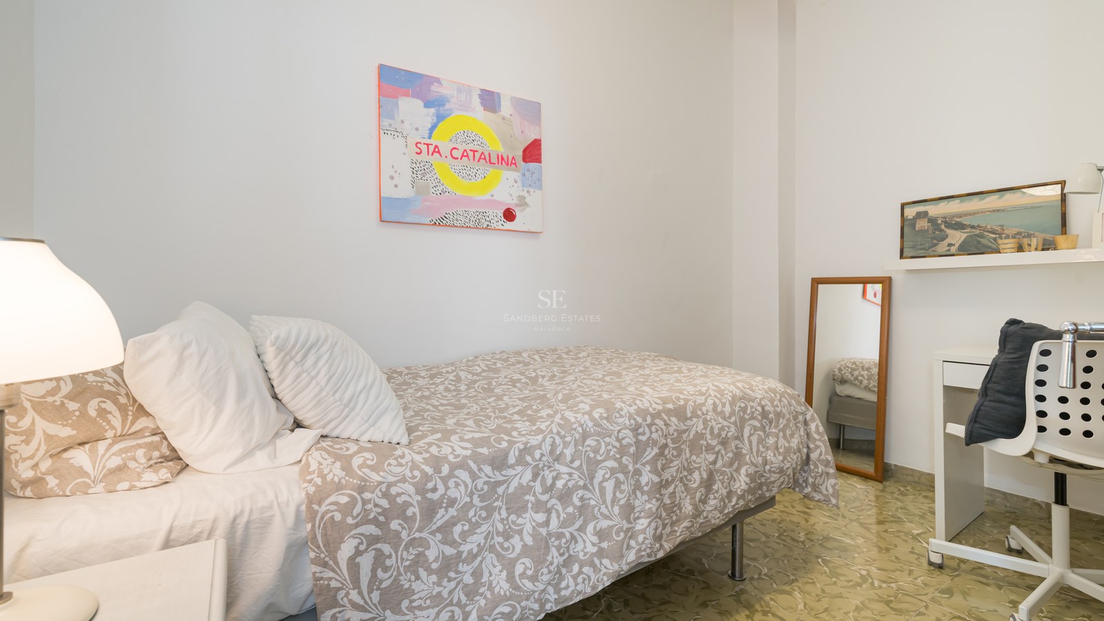 Dormitorio individual luminoso con cama estampada, escritorio blanco y suelo hidráulico tradicional.