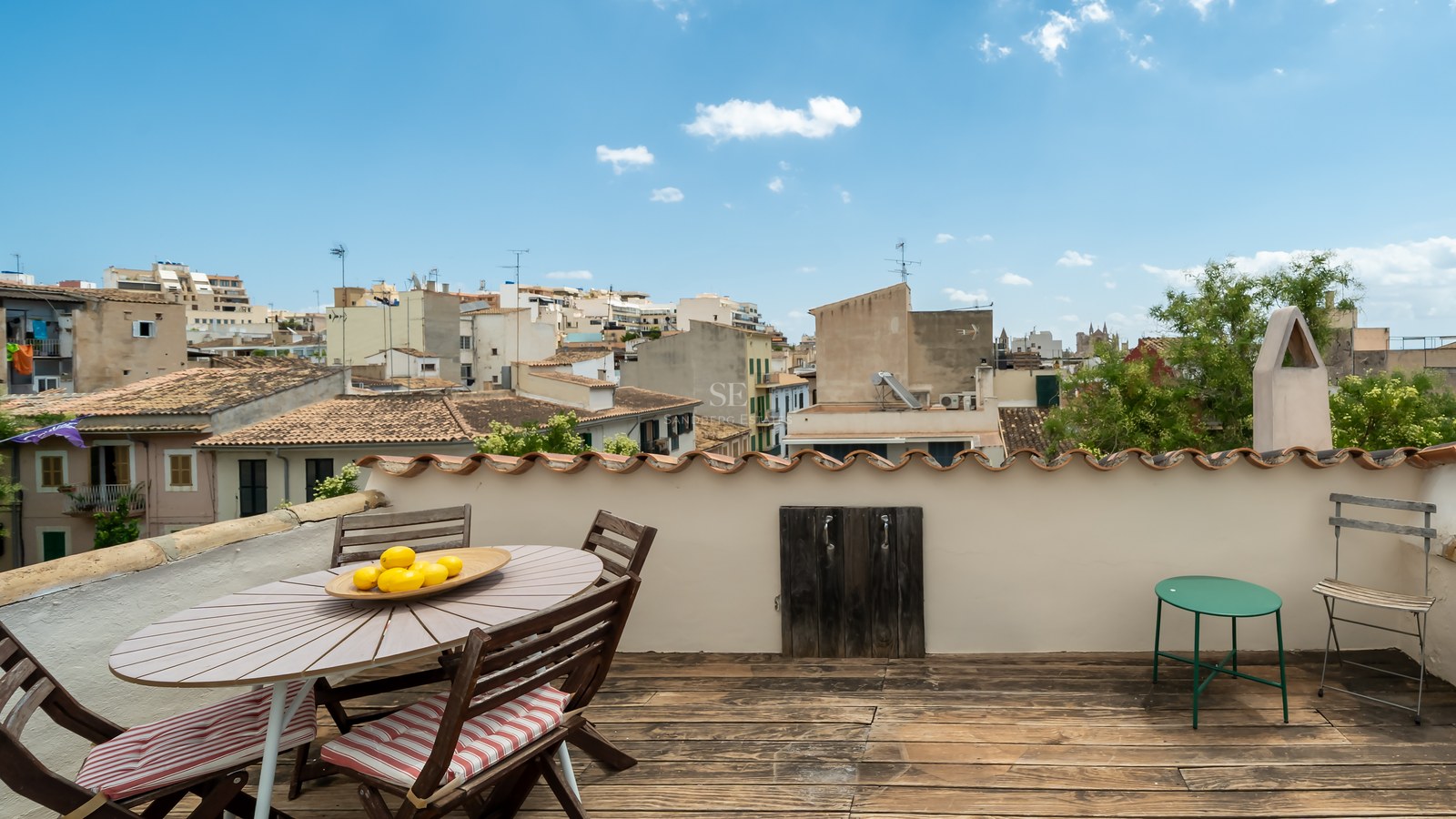 Terraza de madera en azotea con mesa de comedor y vistas panorámicas a los tejados de una ciudad mediterránea.