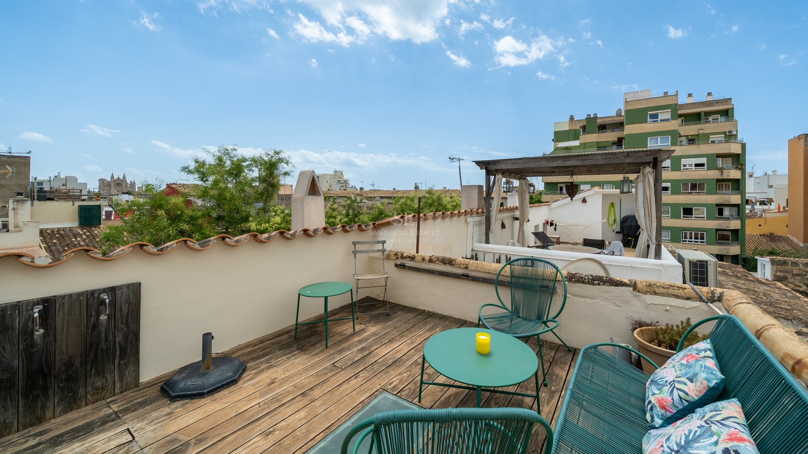 Terraza en azotea con suelo de madera, muebles verde azulado y vistas a la Catedral de Palma.