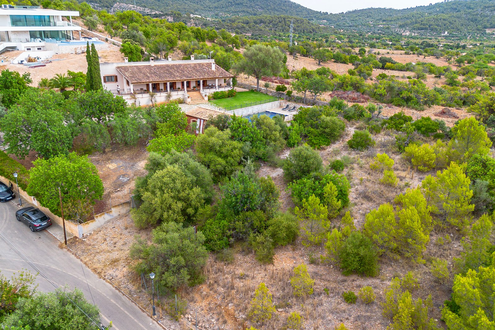 Vue aérienne d'une villa méditerranéenne rustique avec toit en terre cuite, piscine et jardin verdoyant sur les collines.