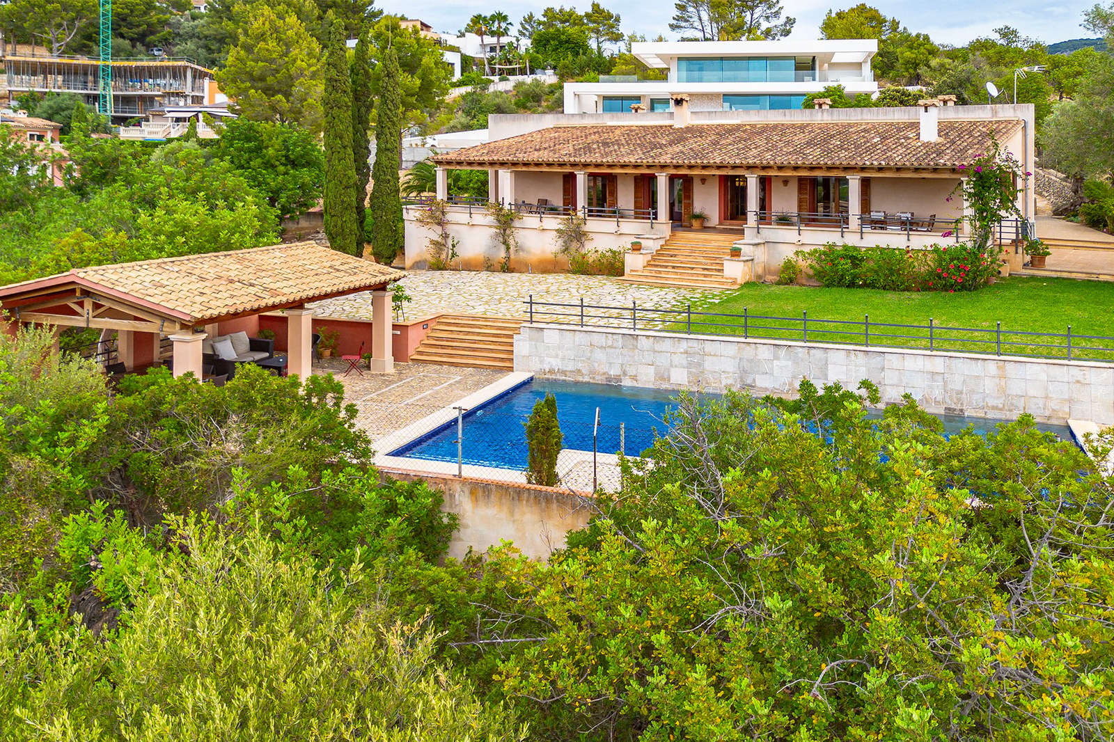 Vue extérieure d'une villa méditerranéenne avec toit en terre cuite, piscine et jardins en terrasses.