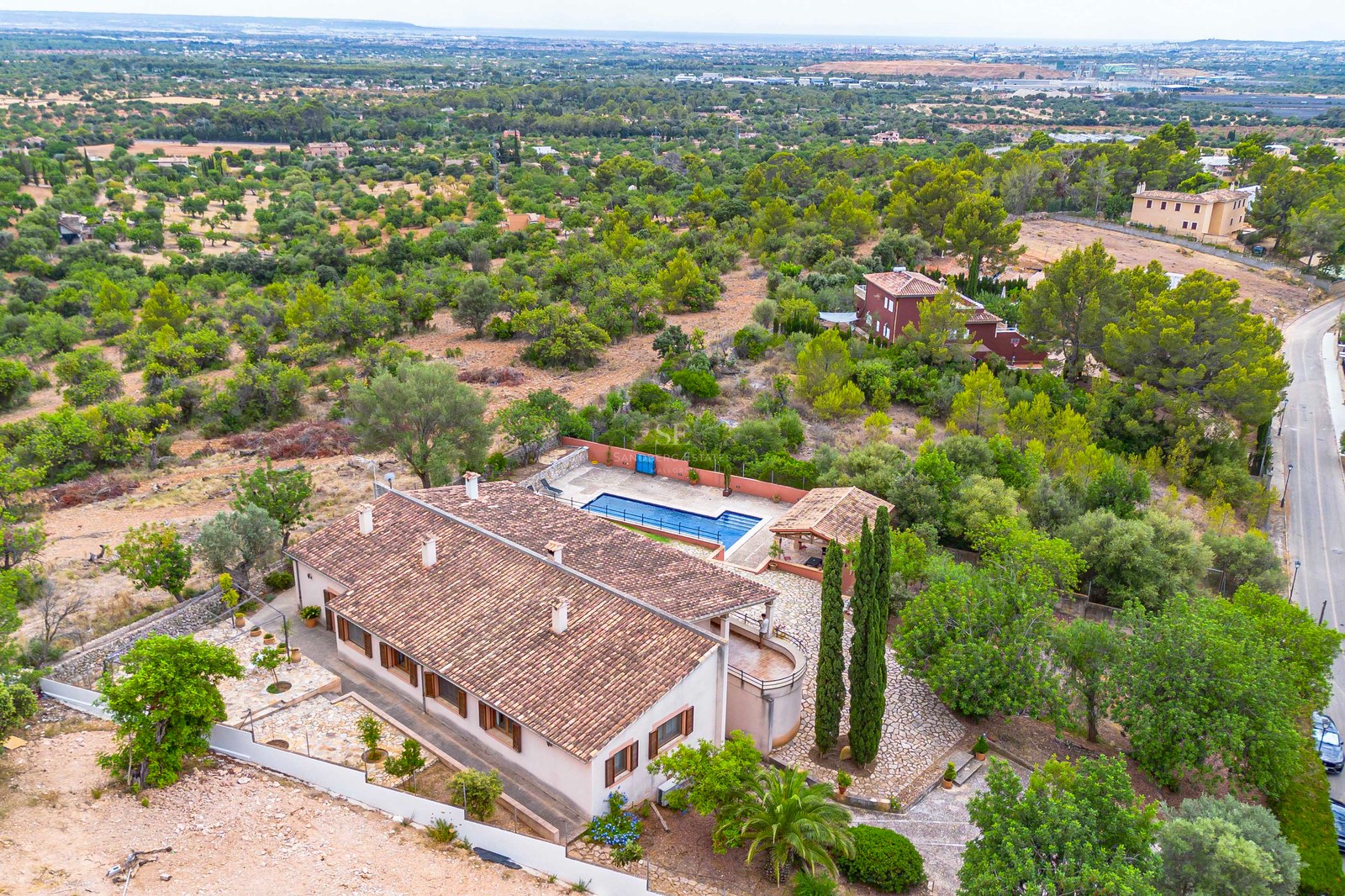 Vue plongeante d'un grand domaine avec une villa au toit de terre cuite, une piscine bleue et un cadre verdoyant.