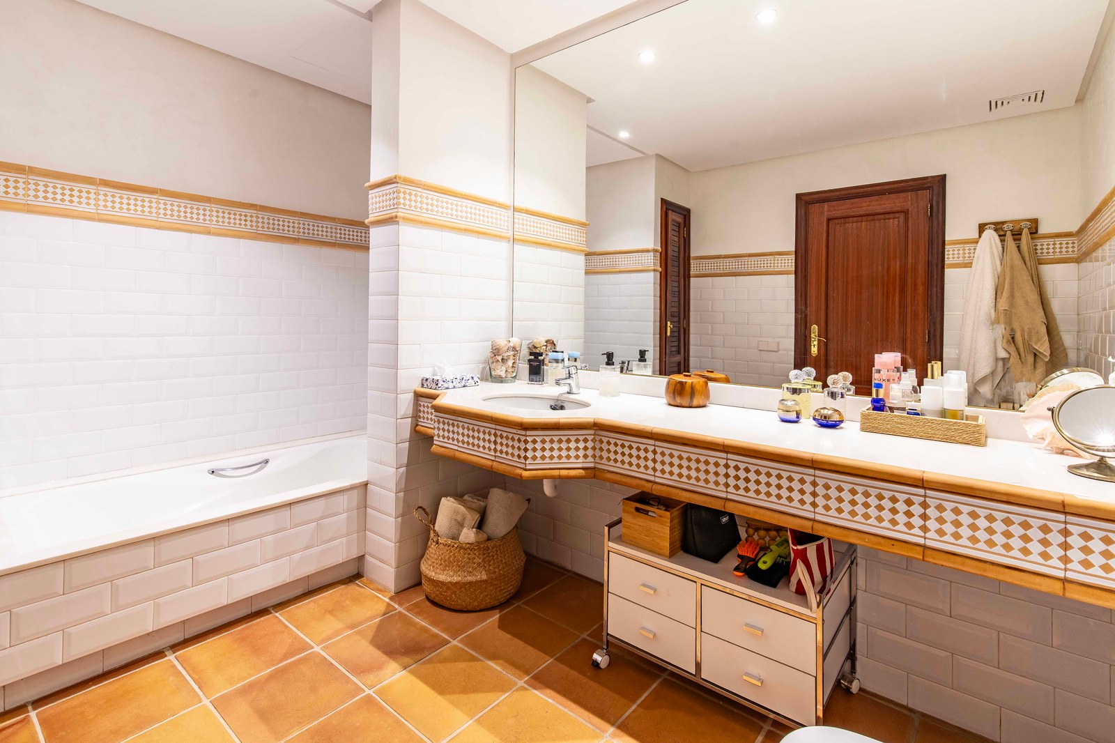 Salle de bain avec carrelage métro blanc, sol en terre cuite, baignoire intégrée et un grand miroir au-dessus du lavabo.