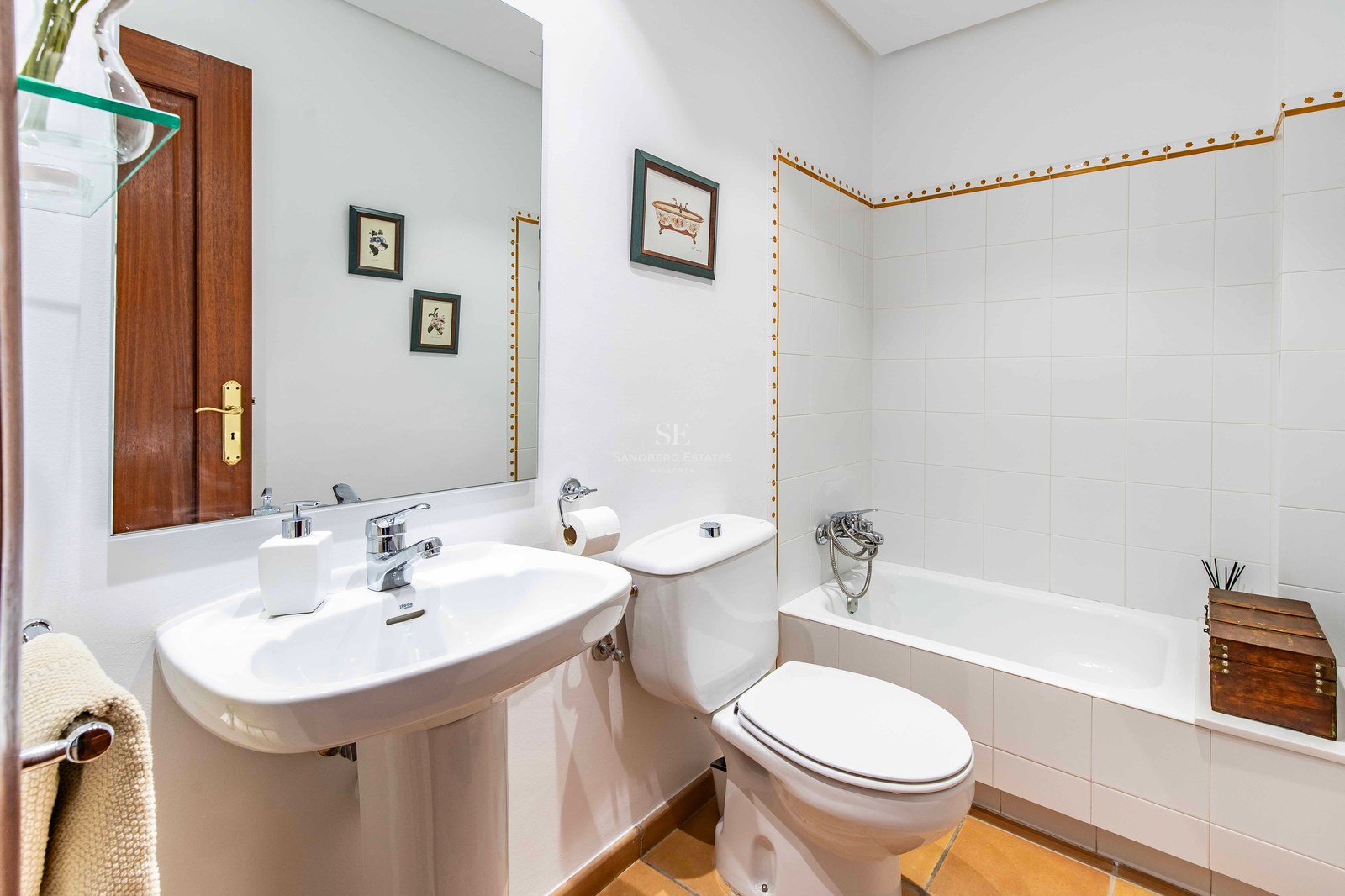 Salle de bain avec carrelage blanc, baignoire, lavabo colonne, toilettes et sol en terre cuite.
